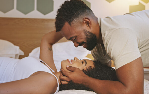 Faces of a loving young couple looking into each other's eyes while lying on a bed at home. Black boyfriend and girlfriend sharing a romantic moment expressing love and affection during time together